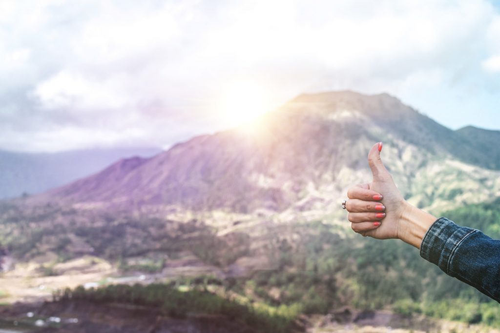 Person giving a thumbs up sign infront of a mountain.