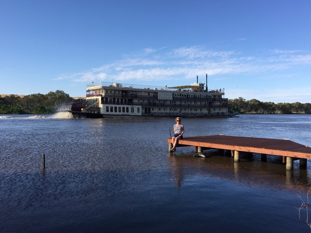 Photograph of Lyn Jefferies on a river jetty with a paddle-steamer in the background