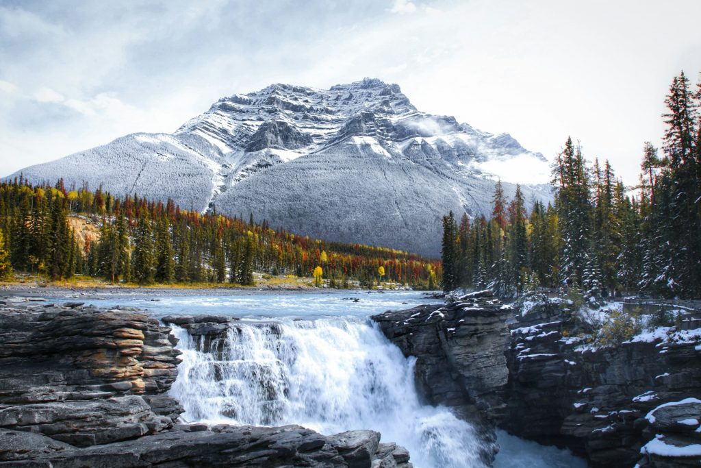 Athabasca Falls in the fall with snow-capped mountains in the background.