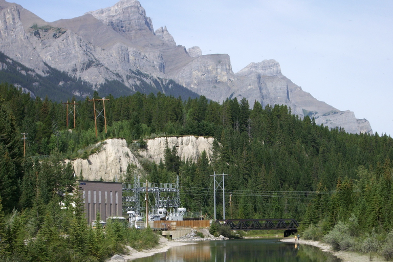 Photograph of a power station and power lines nestled in a valley with mountains in the background.