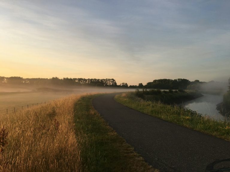 A photograph of a river dyke and field at sunrise