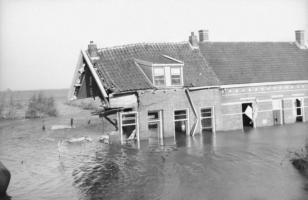 Black and white photograph of a partially submerged and severely damaged house.