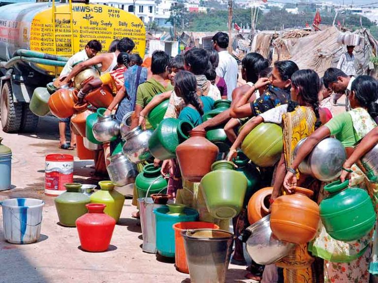 Photograph of people queuing to collect drinking water from a tanker truck.