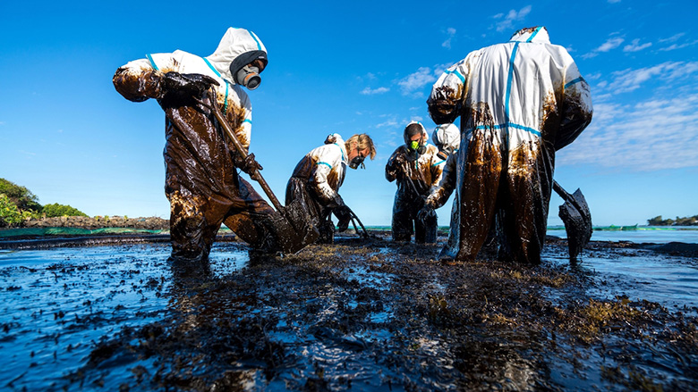 Photograph of people in hazmat suits cleaning up an oil spill.