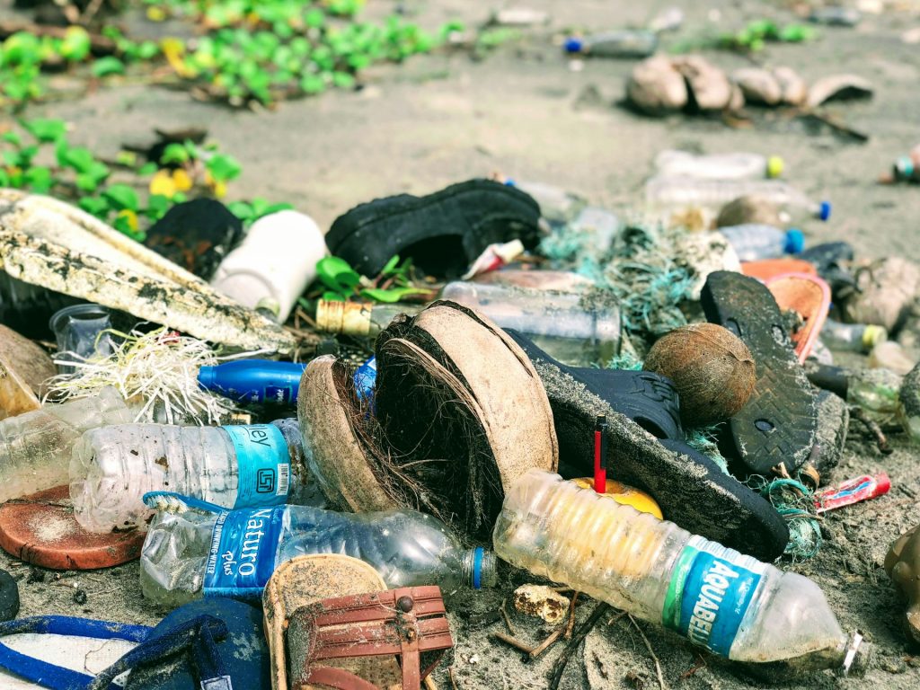 A photograph of waterborne pollution with discarded plastic bottles, sandals, and other rubbish