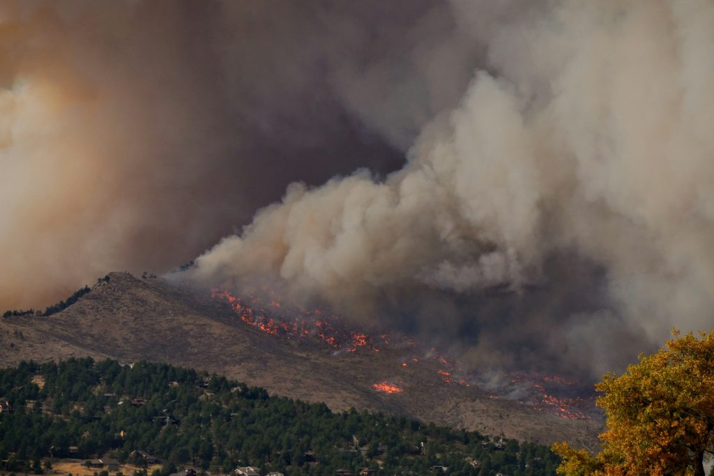 Photograph of a wildfire on the side of a mountain with billowing smoke clouds